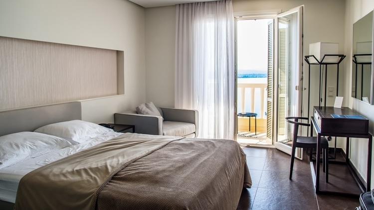 Clean hotel room with balcony door open to show an ocean view for travelers