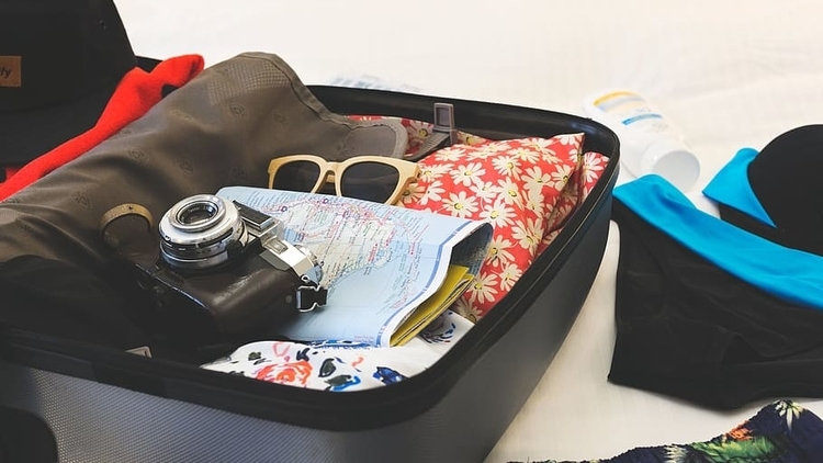 A traveler's open suitcase packed with clothes, a map, sunglasses, a camera and more travel accessories around it